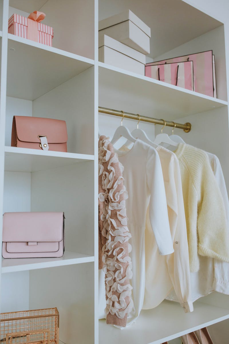 Photo by Anastasia Shuraeva Stylish feminine wardrobe with clothes, bags, and gifts neatly organized on shelves.